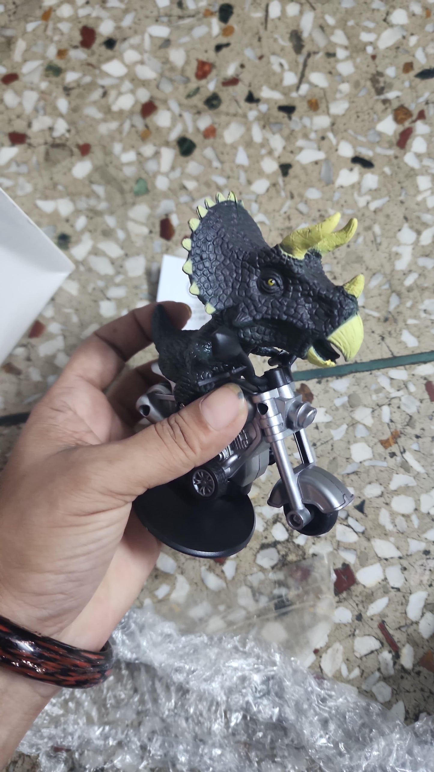 Hand holding a toy dinosaur with a textured floor background