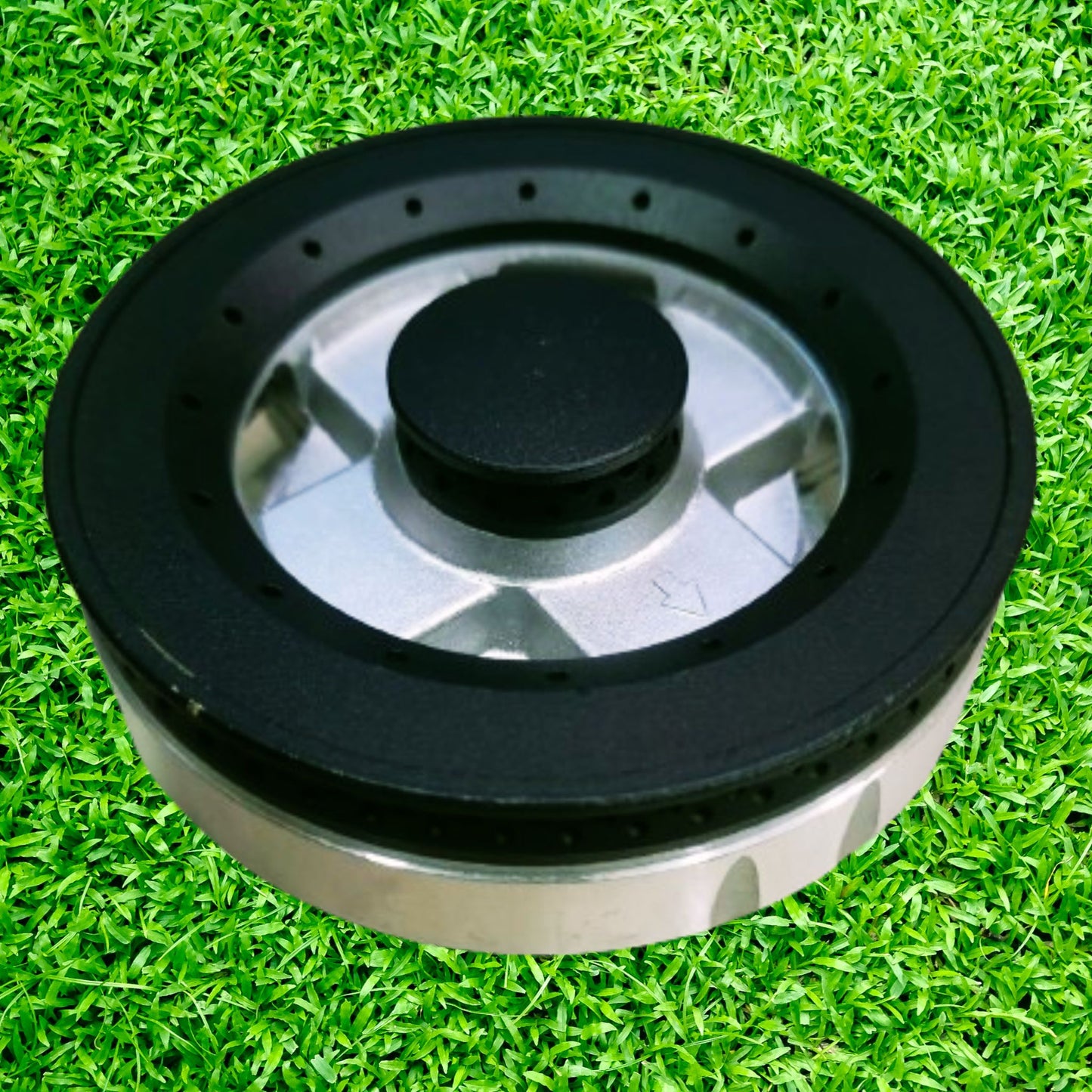 A black Elica gas stove burner with a metallic finish and a central knob, placed on a green grass-like surface.