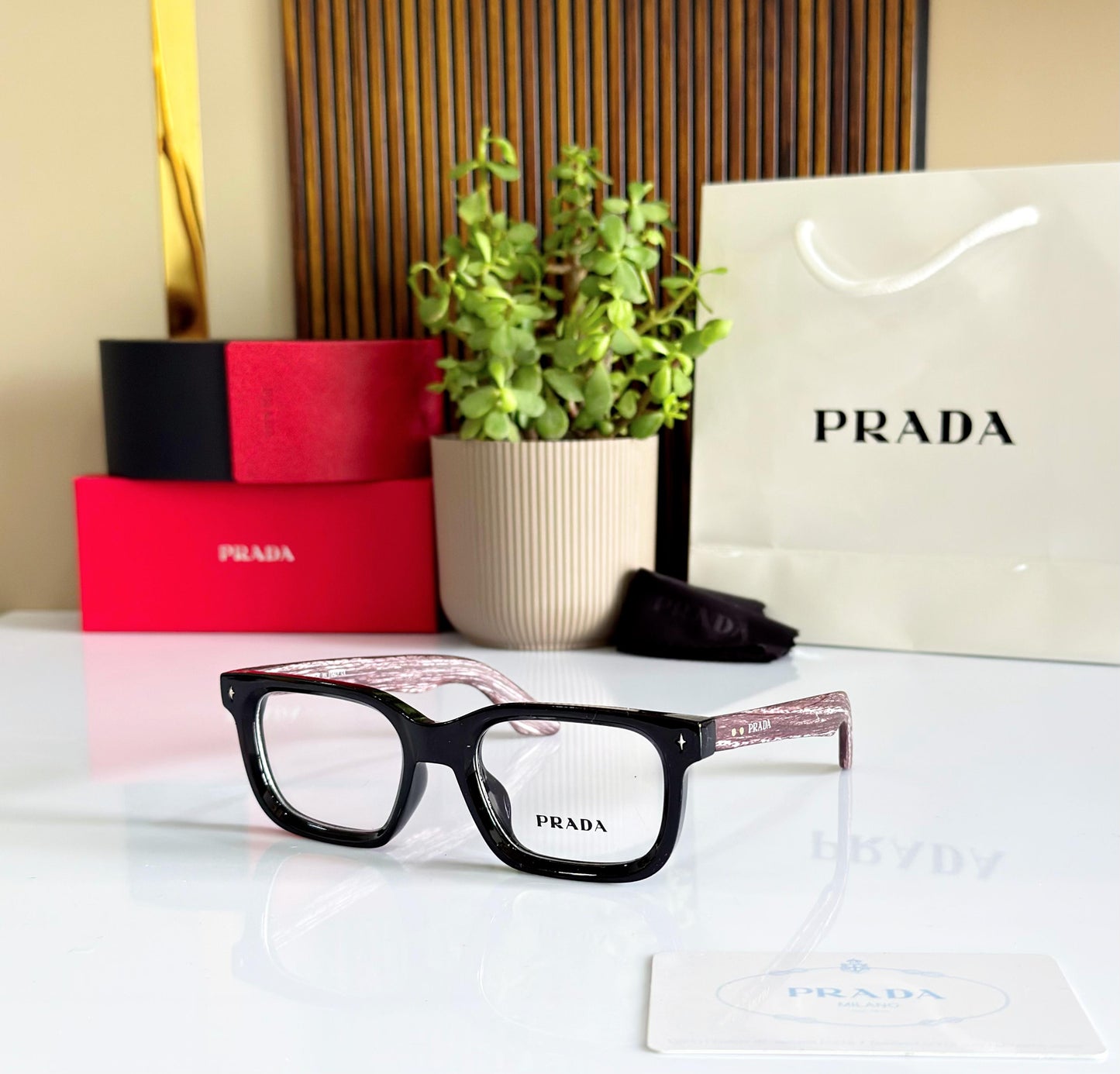 Prada eyeglasses on a table with Prada packaging and a plant in the background.