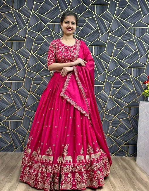 Woman in a pink and red traditional outfit standing against a geometric patterned wall.